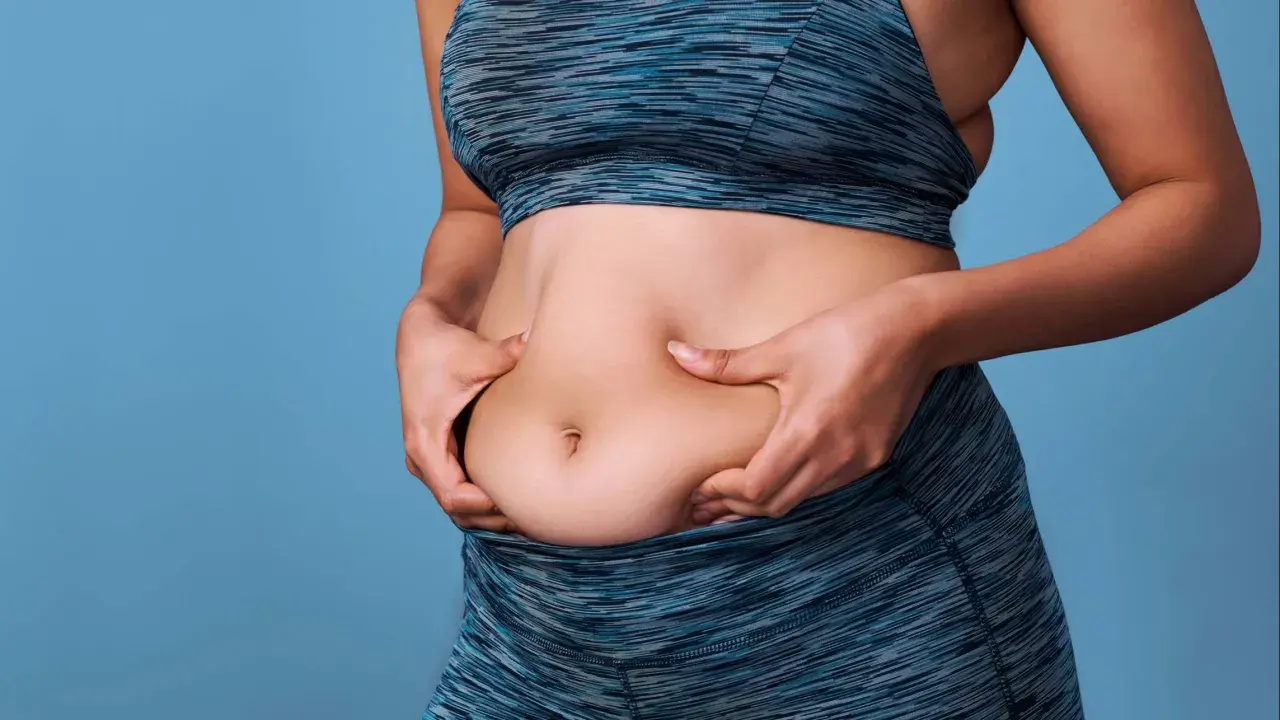 Mujer de 50 años se pellizca el abdomen, buscando perder grasa abdominal.