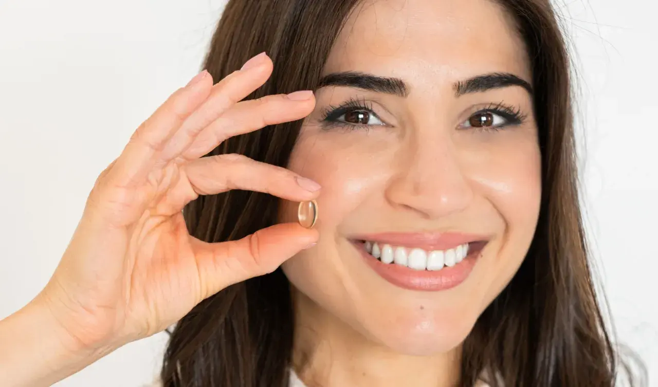 Mujer sonriente muestra una cápsula de omega 7, un aliado para quienes buscan adelgazar de forma natural.