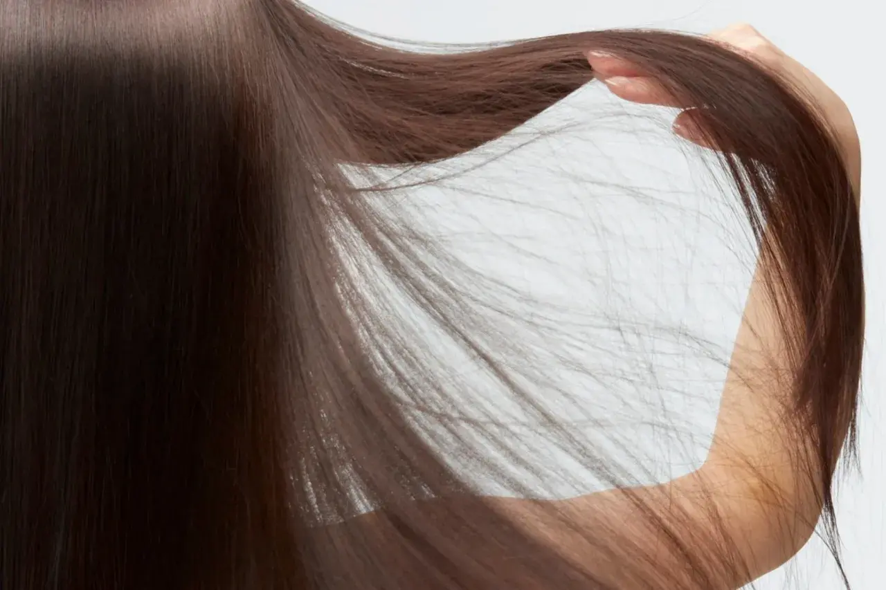 Detalle de pelo fino y escaso de mujer, con mechones sueltos que caen sobre su brazo.
