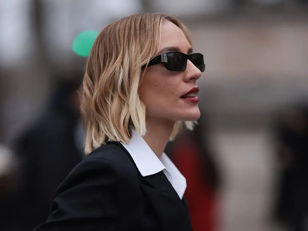 Mujer con melena corta rubia, gafas de sol y traje negro. Cortes de pelo melena corta modernos y chic.