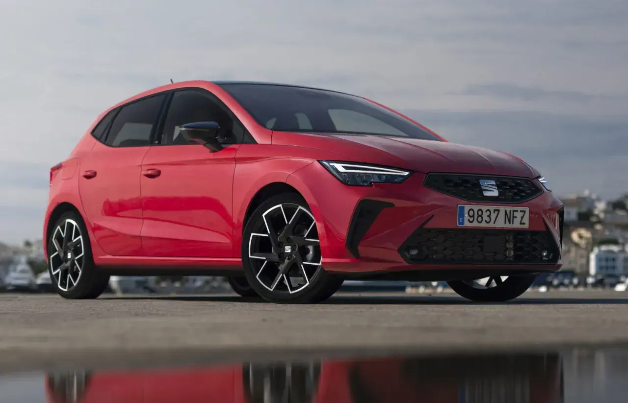 Un Seat Ibiza rojo vibrante, uno de los modelos más icónicos, posa con estilo frente a un paisaje urbano.