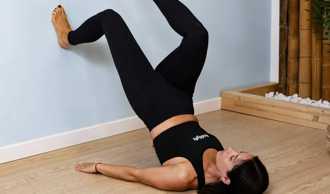 Mujer realizando ejercicios abdomen bajo, con los pies apoyados en la pared y el cuerpo elevado.