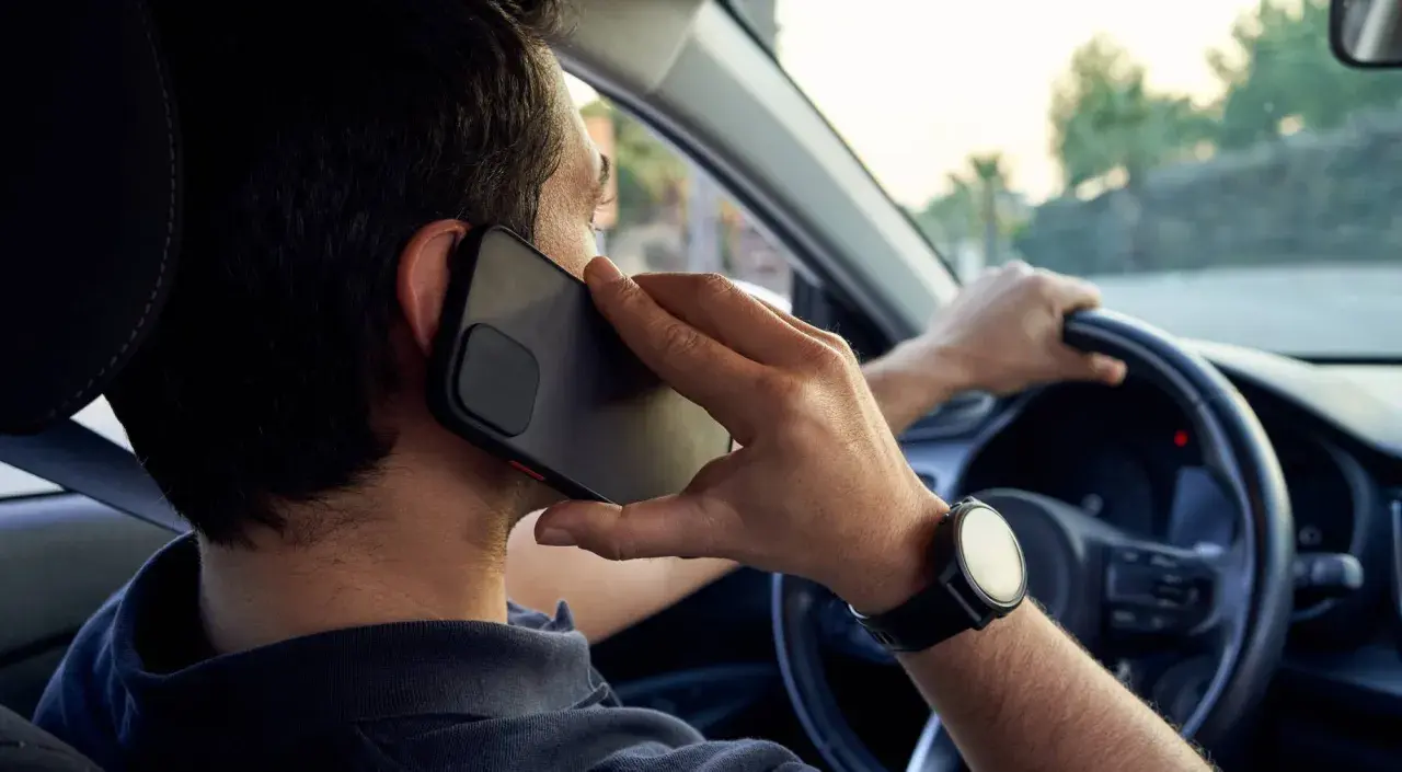 Hombre hablando por teléfono mientras conduce, una acción que puede llevar a conducir de forma temeraria.