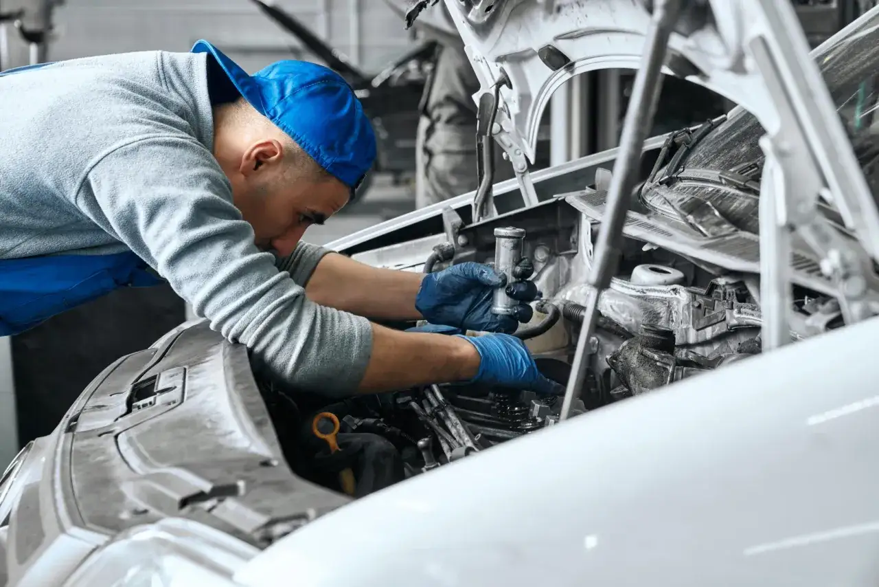 Mec&aacute;nico con guantes azules realiza mantenimiento a coche gasolina, revisando el motor abierto.