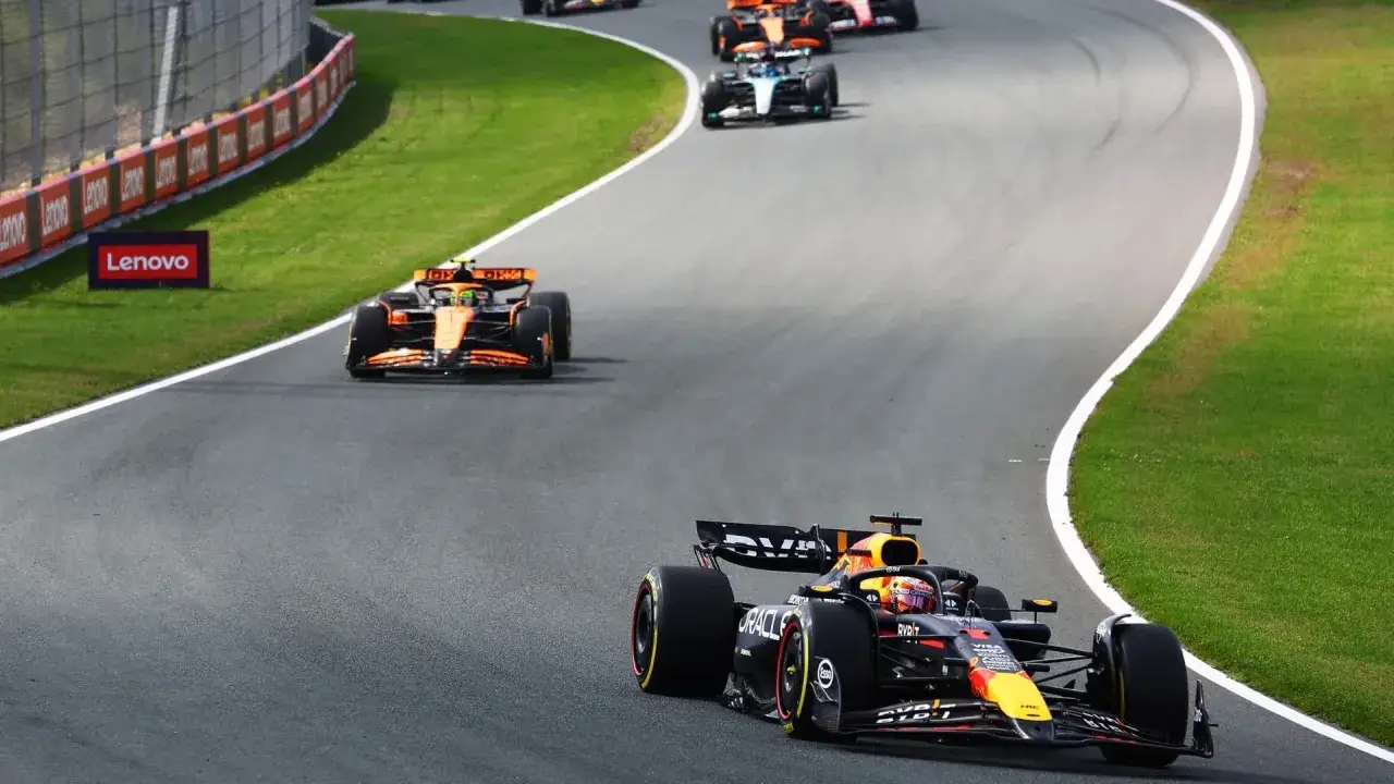 Coches de F&oacute;rmula 1 compiten en una carrera al sprint. El coche Red Bull lidera, seguido por un McLaren naranja.