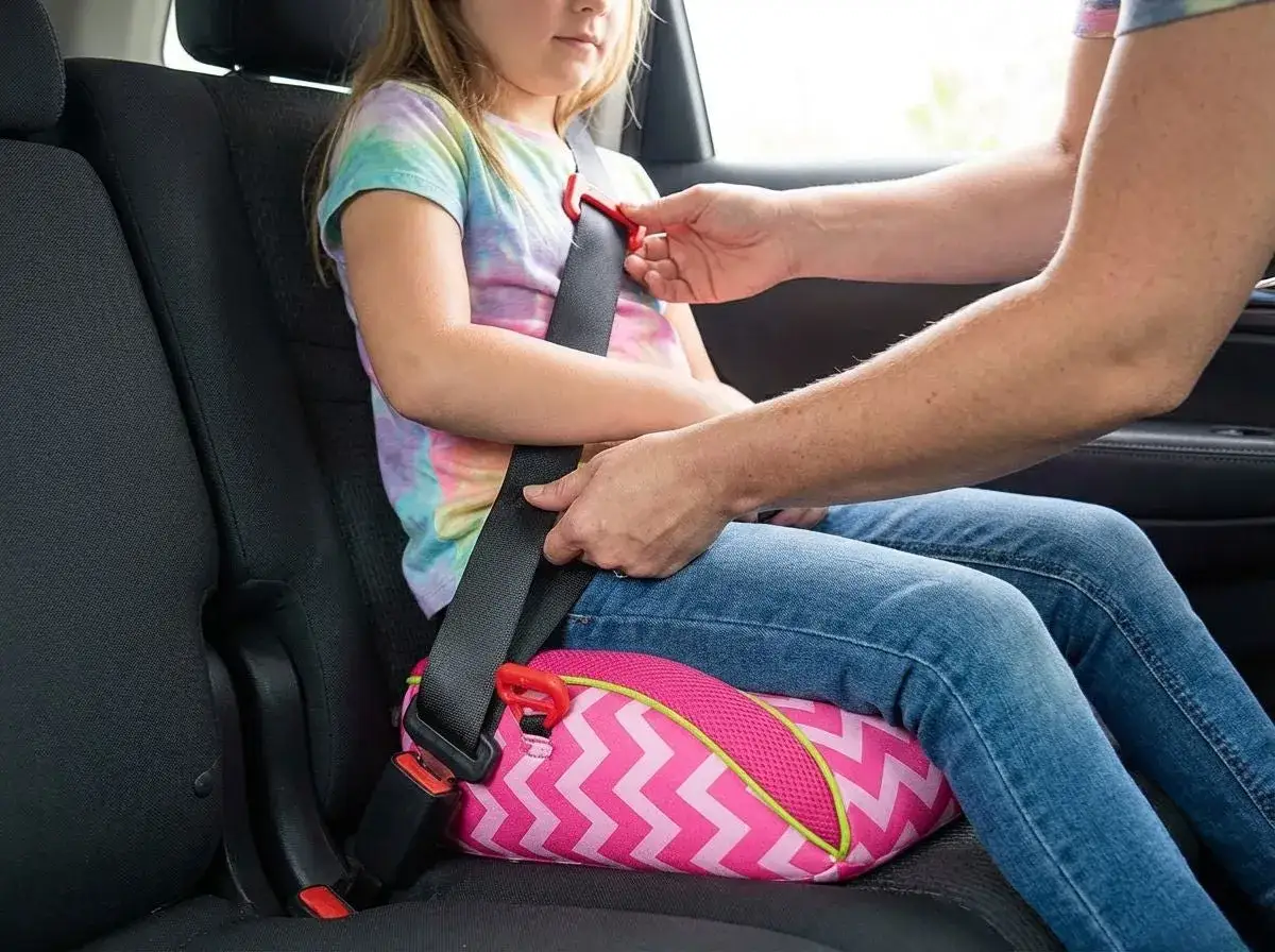 Ni&ntilde;a sentada en un alzador coche, asegurando el cintur&oacute;n. Cumple la normativa de seguridad vial para ni&ntilde;os.