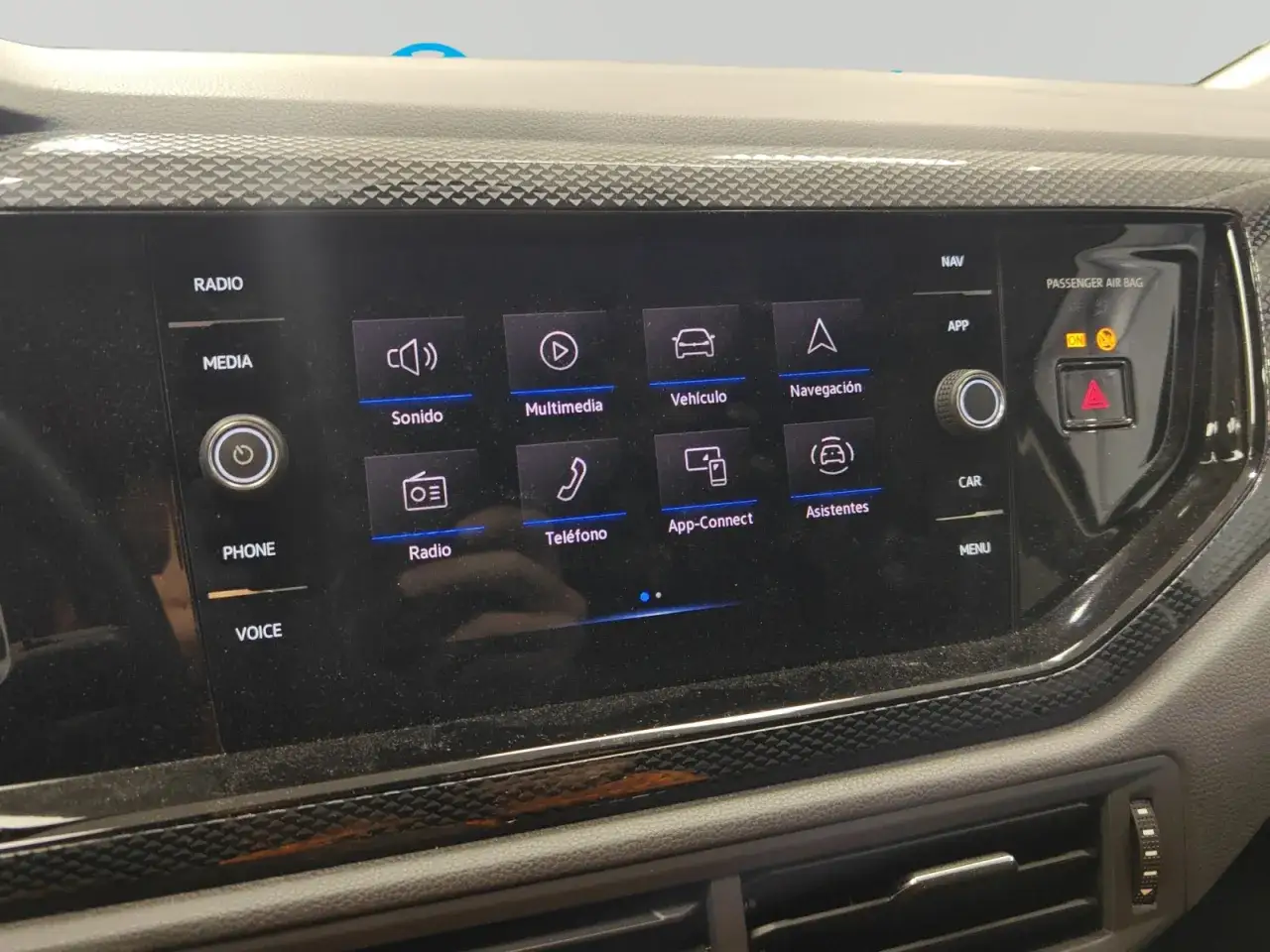 Pantalla t&aacute;ctil de un Volkswagen Taigo con iconos de radio, multimedia, veh&iacute;culo, navegaci&oacute;n, tel&eacute;fono, App-Connect y asistentes. La luz de airbag est&aacute; encendida, indicando posibles problemas.