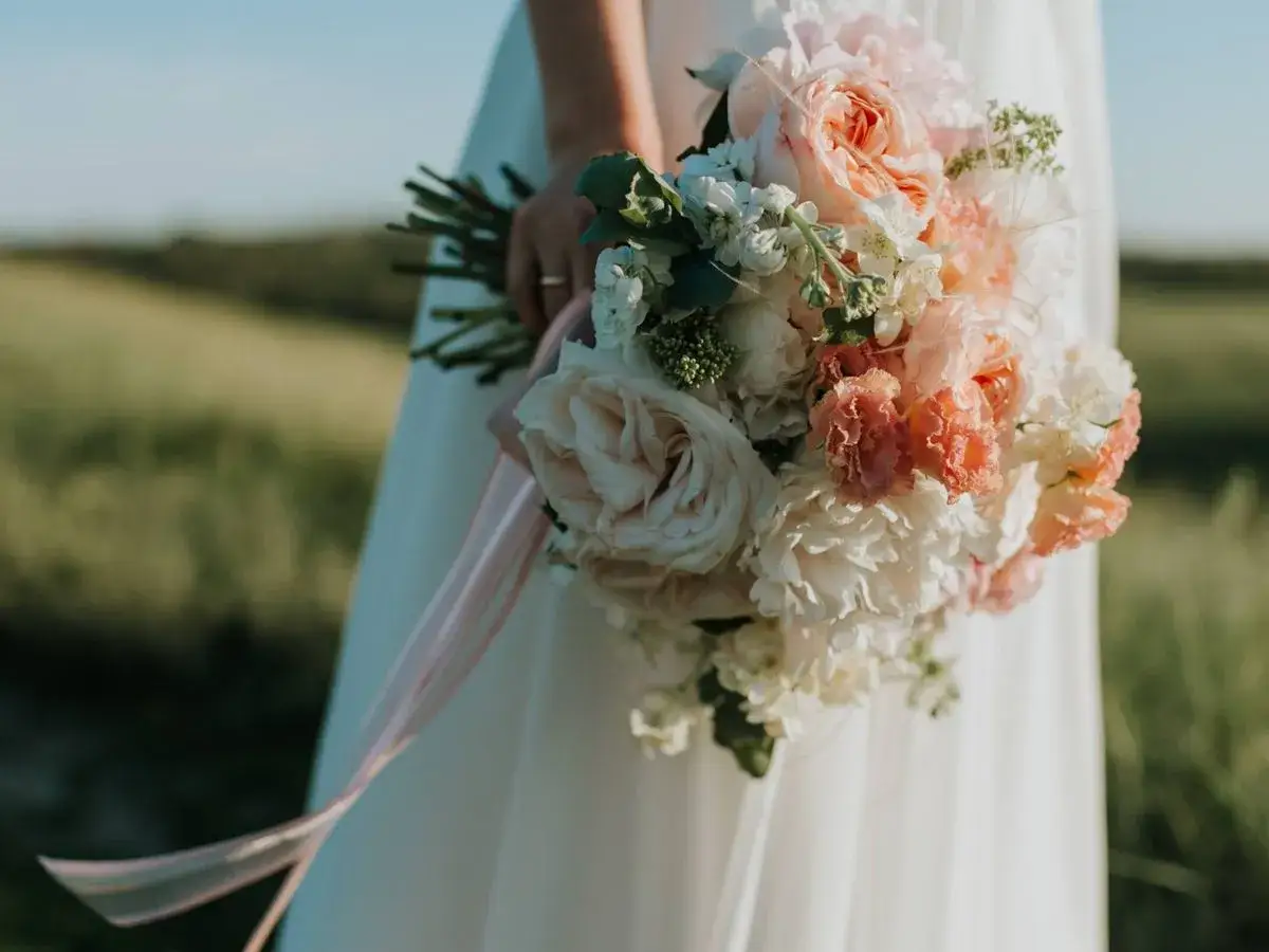 Un ramo de novia con rosas y peonías en tonos pastel, la última tendencia en ramos de novia, con cintas de seda cayendo.