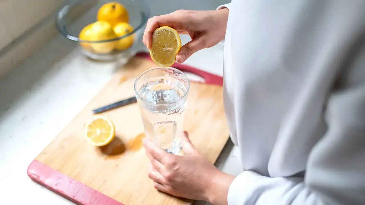 Mano exprime un lim&oacute;n en un vaso de agua. En la tabla de cortar hay otro medio lim&oacute;n y un cuchillo.
