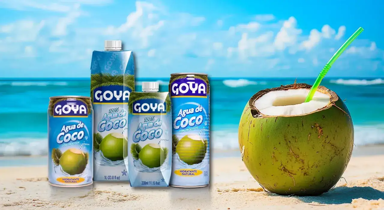 Disfruta del refrescante sabor del agua de coco Goya en latas y cartones, con un coco abierto listo para beber en la playa.