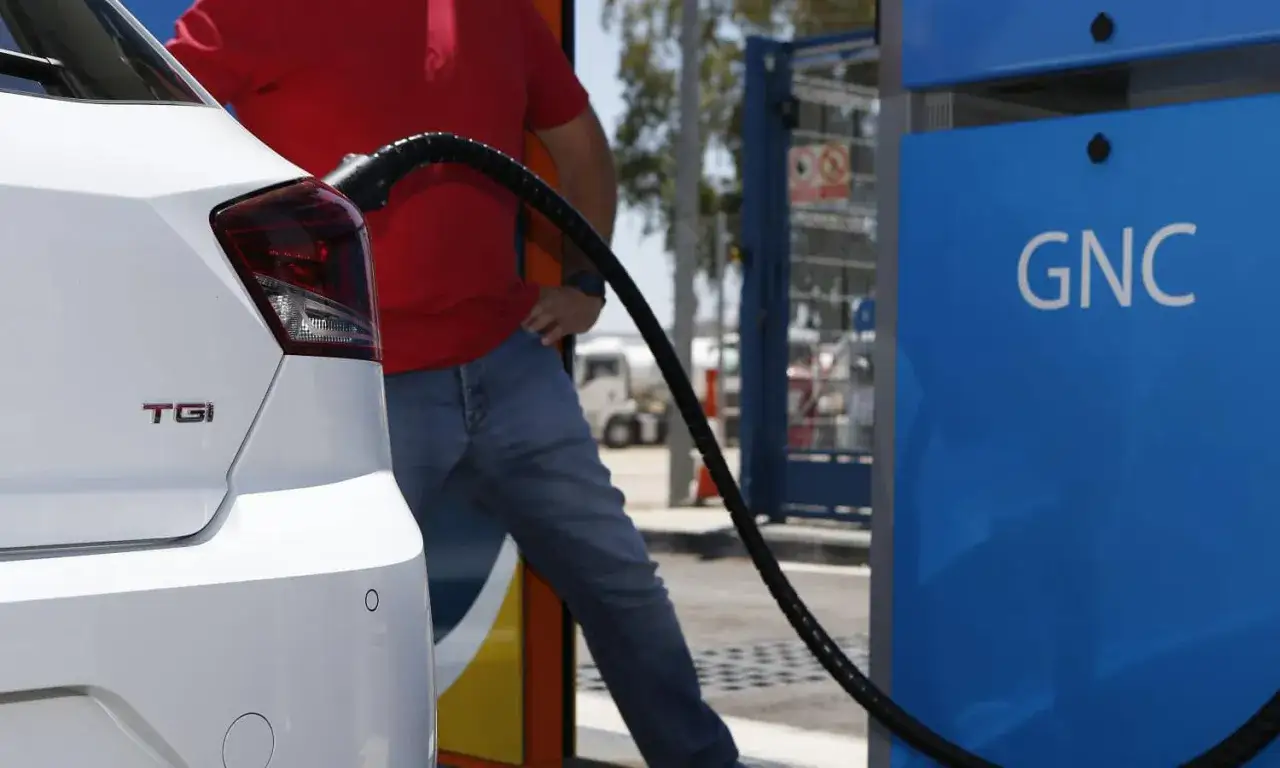 Un coche blanco con la insignia TGI se está repostando en una estación de GNC.