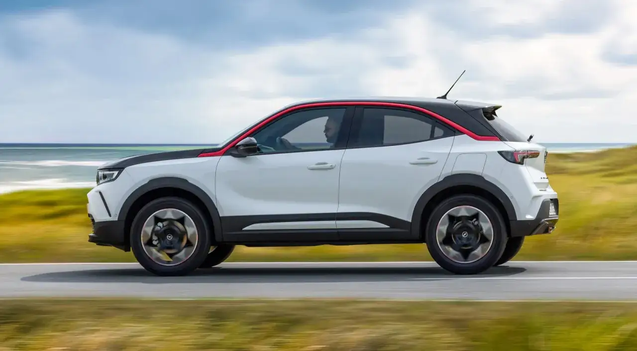 Un Opel Mokka blanco con detalles rojos recorre una carretera costera. Las opiniones sobre este coche son muy positivas.