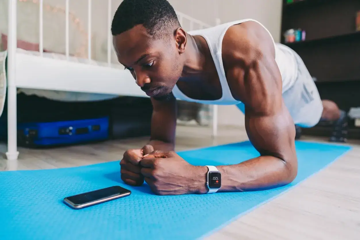 Hombre haciendo plancha en casa, usando su reloj inteligente para seguir su rutina. &iexcl;Perfecto para las mejores app ejercicio en casa gratis!