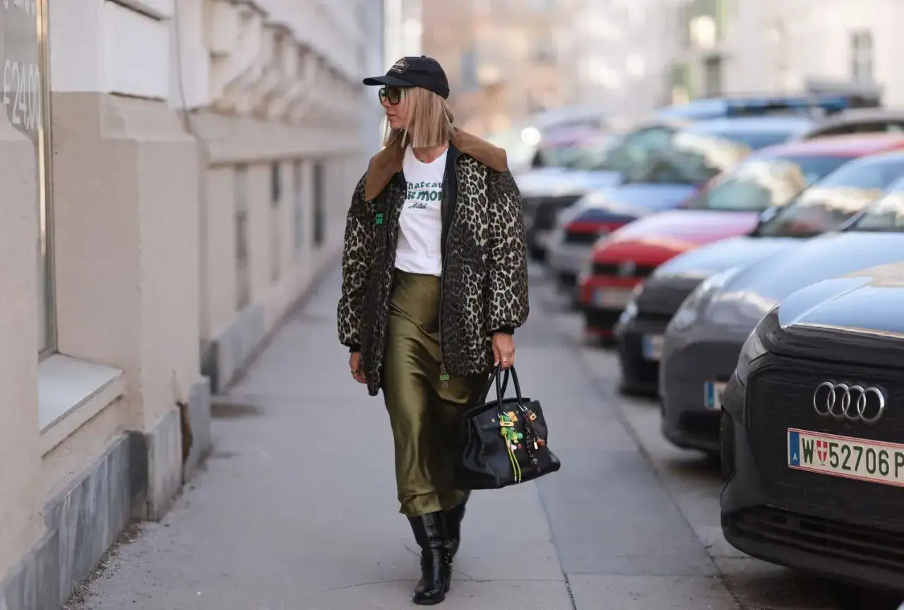 Mujer con chaqueta de leopardo y falda satinada verde olivo, botas negras y bolso negro con adornos.
