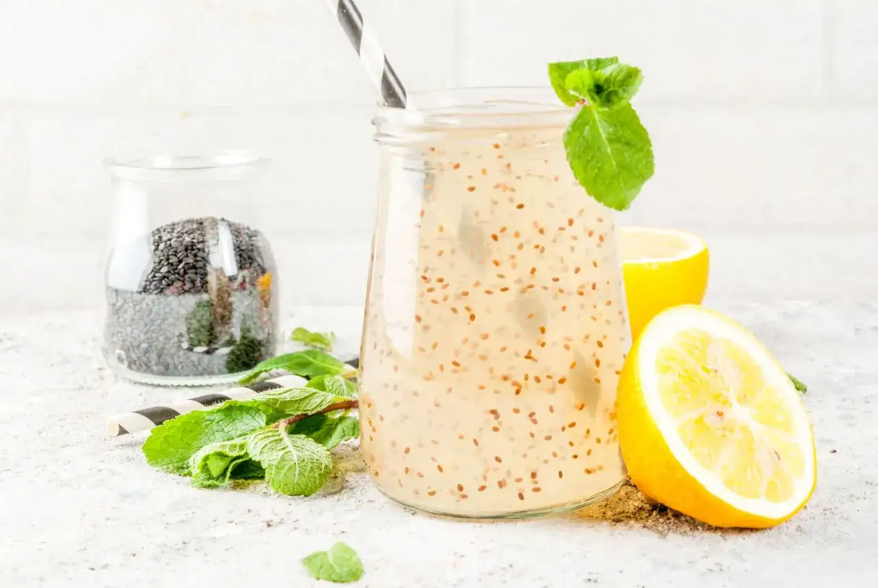 Refrescante agua de chia con lim&oacute;n y menta, lista para disfrutar. Un tarro de semillas de chia al fondo.