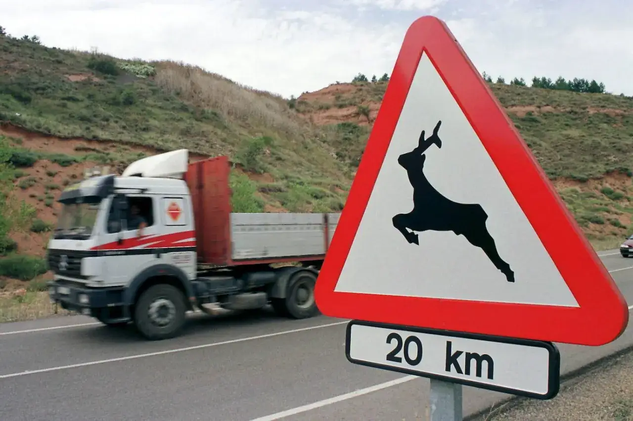 Se&ntilde;al de advertencia de animales salvajes con silueta de ciervo saltando. Un cami&oacute;n pasa por la carretera.